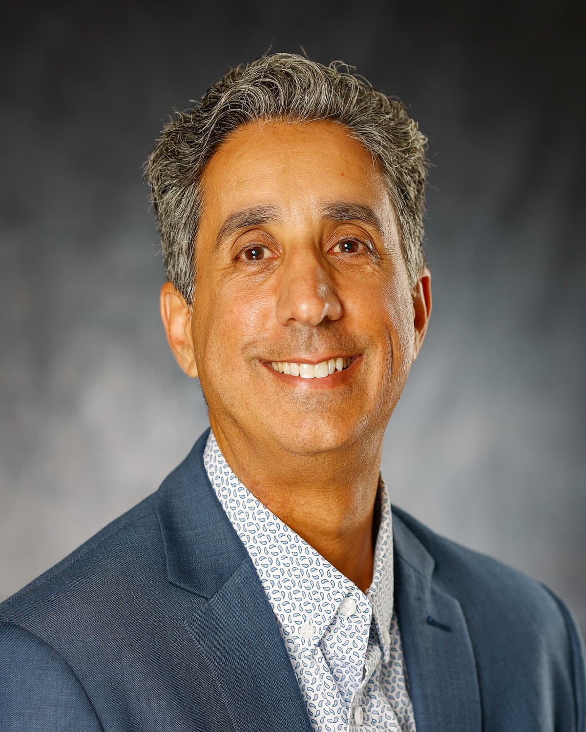 Smiling man with gray hair in a blue blazer and patterned shirt in a studio headshot