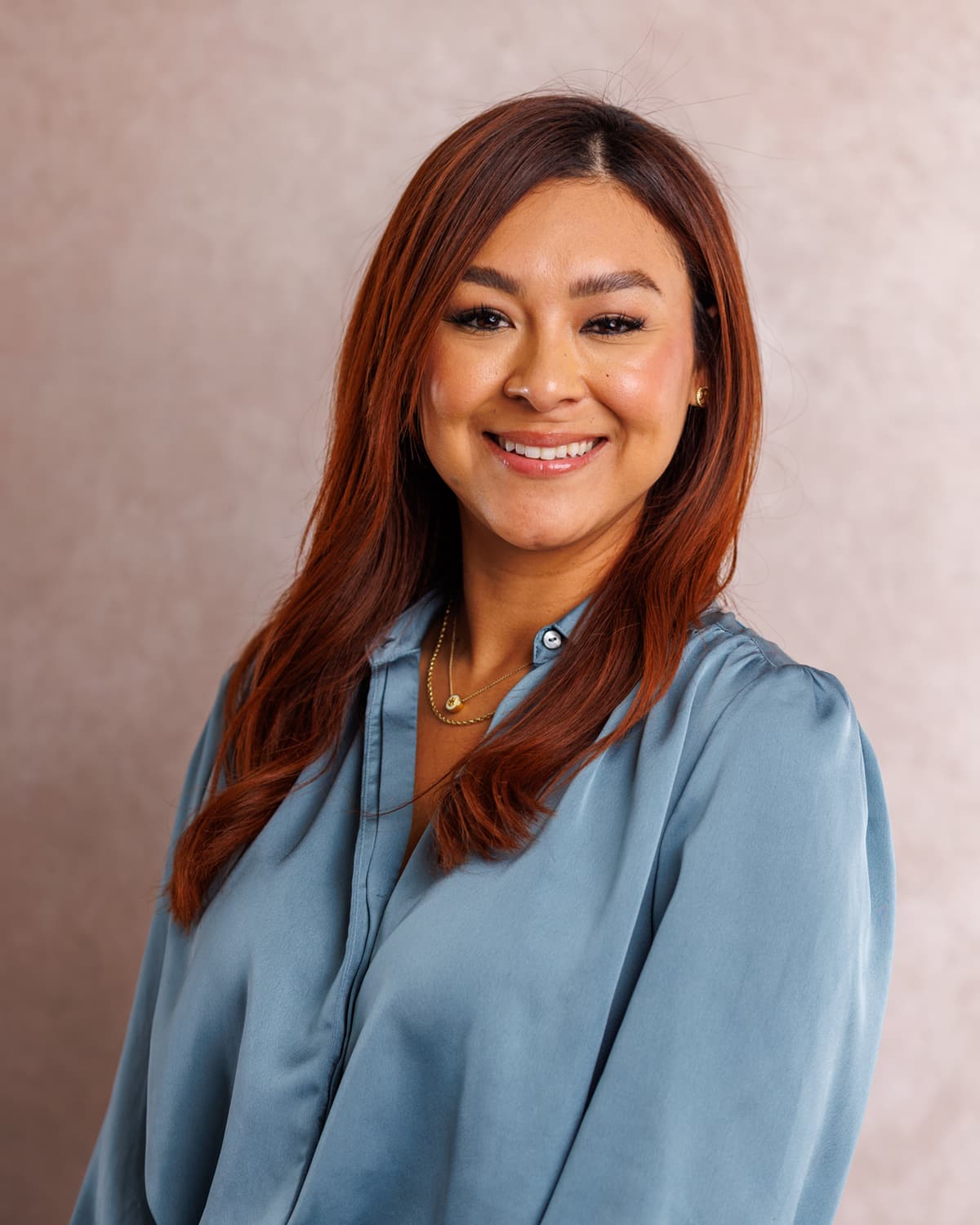 Smiling professional in a blue satin blouse in a studio headshot against a soft blush backdrop