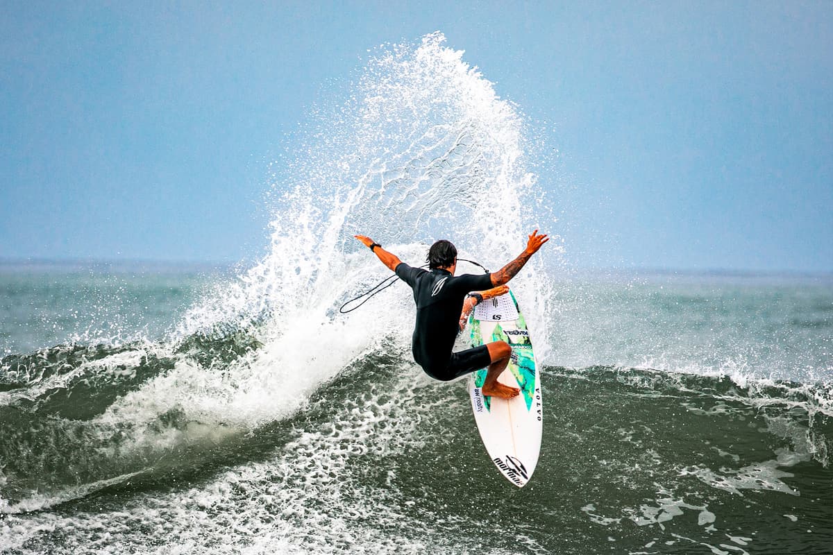 Surfer in a black wetsuit launching off a wave in a burst of spray