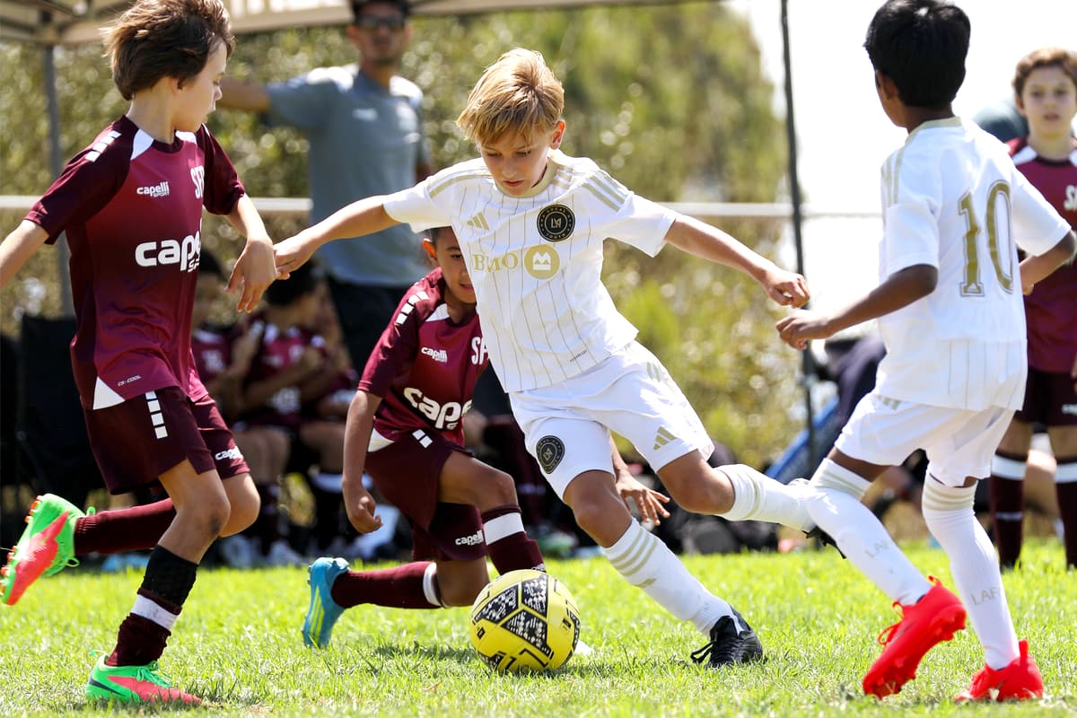 Youth soccer players in white and maroon uniforms competing for the ball during a match